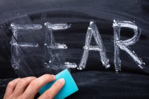 Hand Erasing Fear Word With Blue Sponge On Blackboard